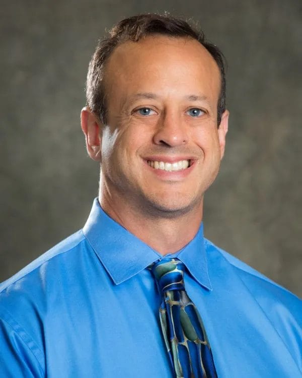 Smiling man in a blue shirt and tie at Scale Community Events, showcasing professional networking opportunities.
