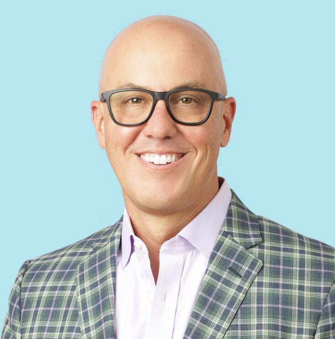Headshot of a smiling person in glasses and a plaid jacket, only available at Scale Community Events.